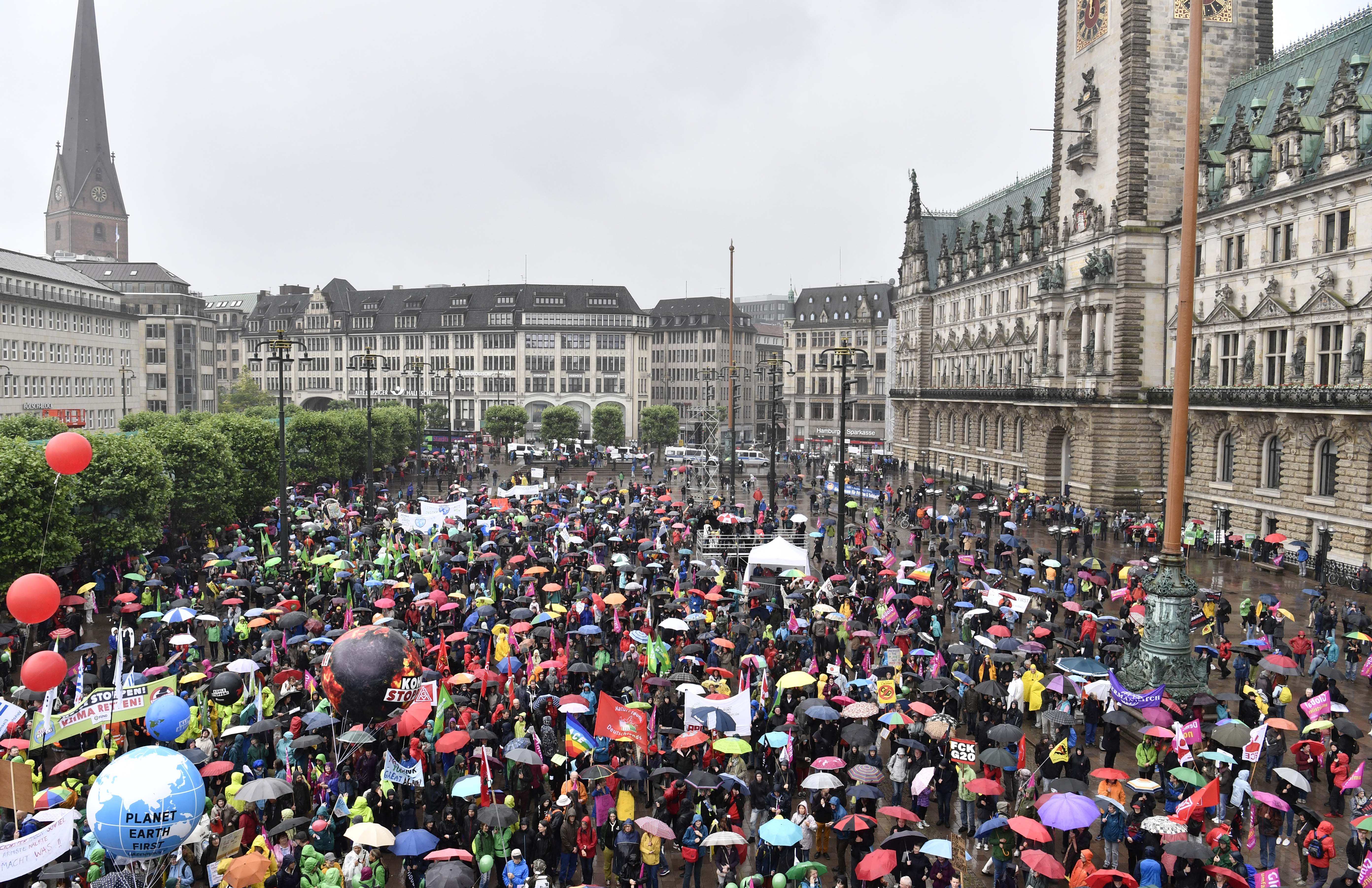 Participants hold placards during a demonstration in front of the Hamburg city hall (Rathaus) called by several NGOs ahead of the G20 summit in Hamburg on a rainy July 2, 2017. / AFP PHOTO / John MACDOUGALL