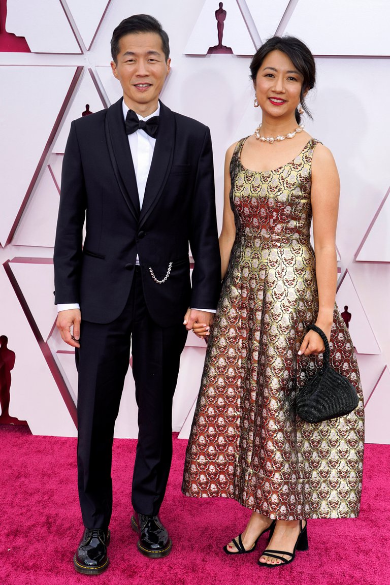 Lee Isaac Chung con un impecable black tie asistió a la ceremonia de los Oscar 2021 con Valerie Chung, quien lució un vestido al tobillo con breteles gruesos, mini bag y zapatos negros de taco cuadrado.